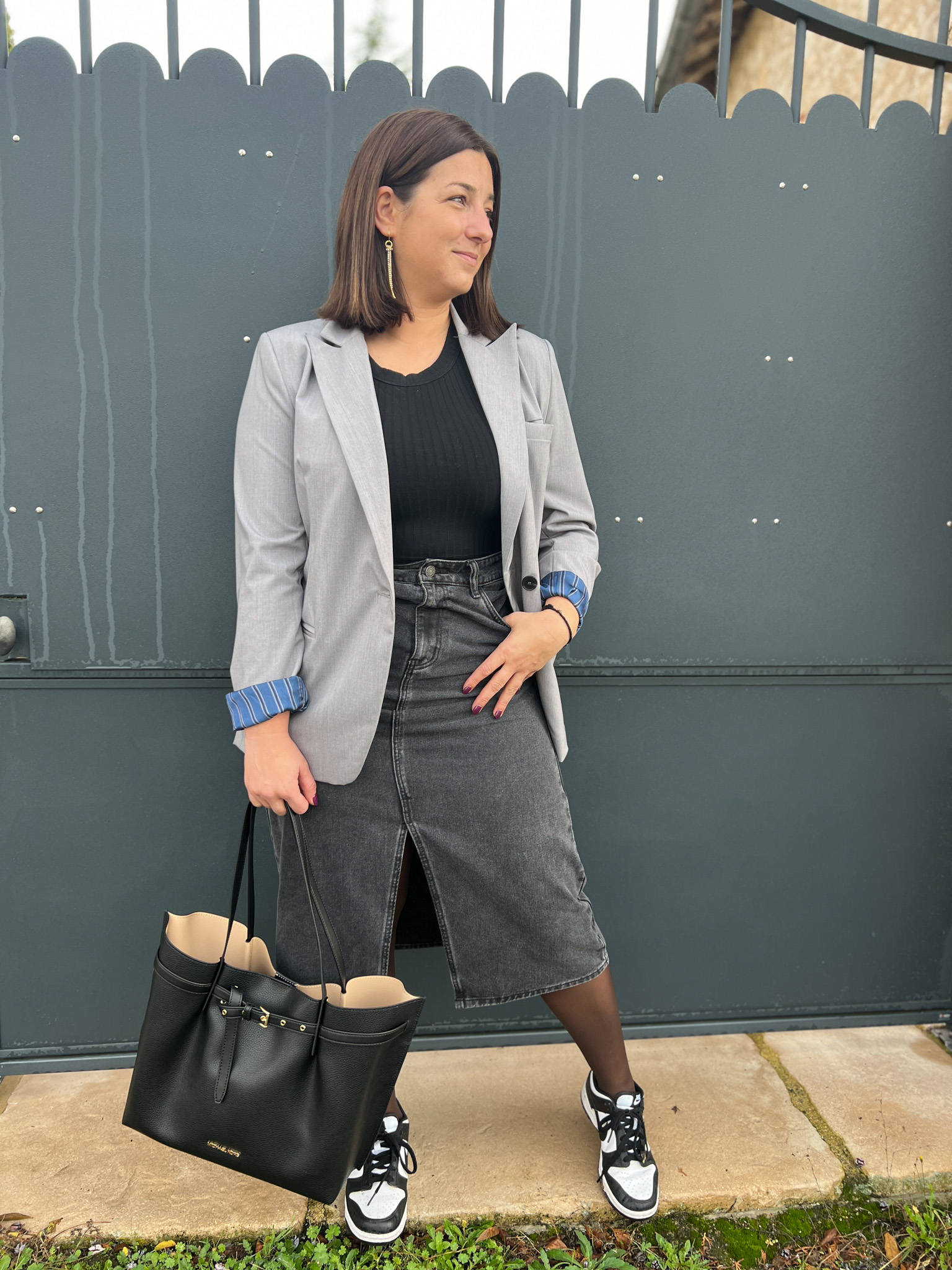 look jupe en jean grise longueur midi portée avec un top noir et un blazer gris. Le look est porté avec une paire de baskets nike dunk et un sac cabas noir 