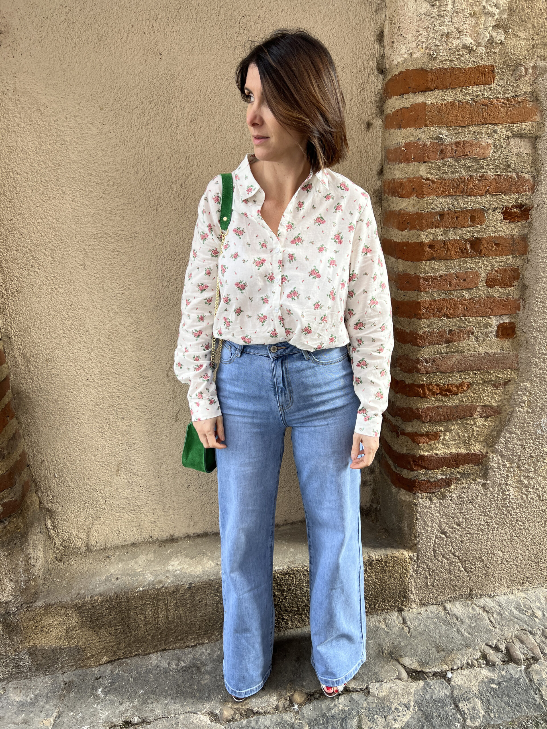 Chemise fleurie à manches longues portée avec jean et sac à main vert. La chemise a une coupe droite et se ferme par boutons sur le devant.